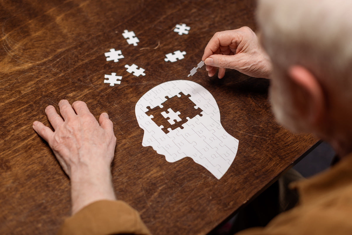Gehirn-Alterung stoppen - Senior spielt Puzzle in Gehirnform auf Holztisch